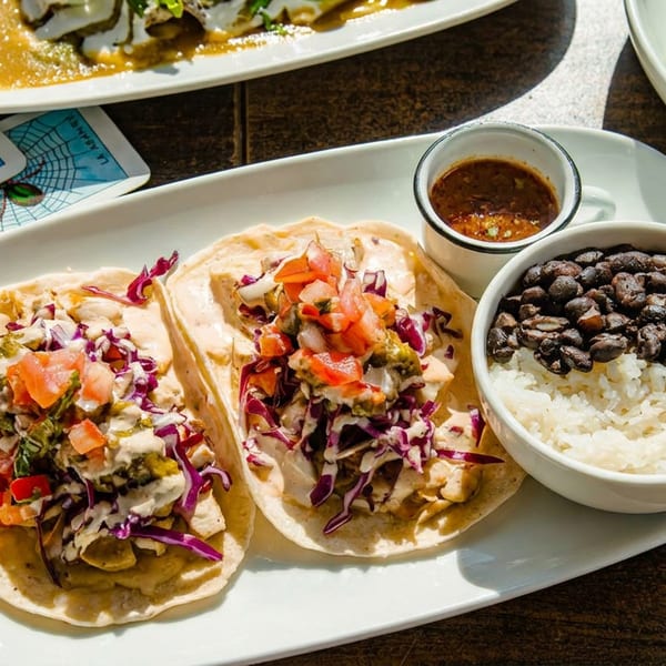 Three tacos with red cabbage, pico de gallo, and sauce, served with rice and black beans.