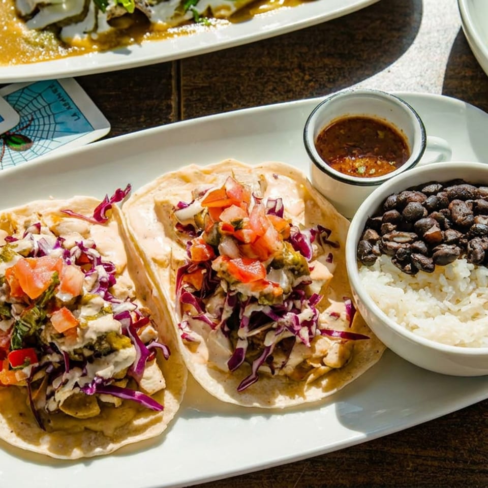 Three tacos with red cabbage, pico de gallo, and sauce, served with rice and black beans.