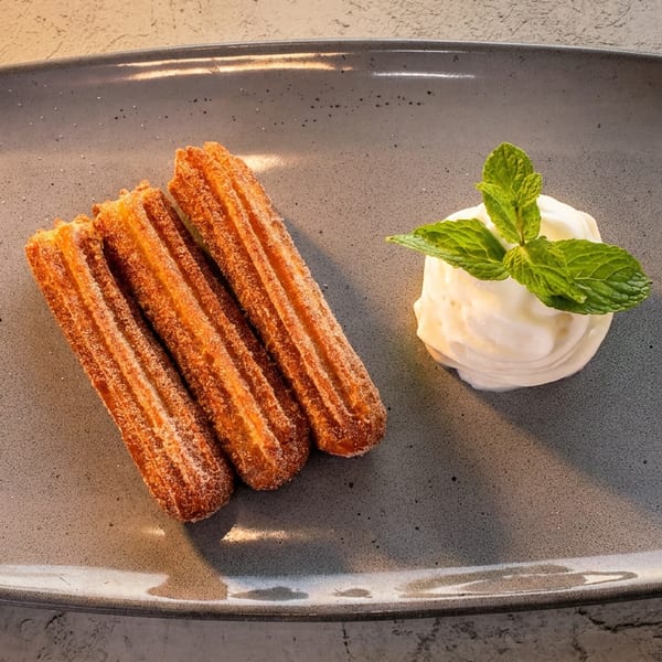 Three churros dusted with cinnamon sugar, served with a scoop of vanilla ice cream and mint on a gray plate.